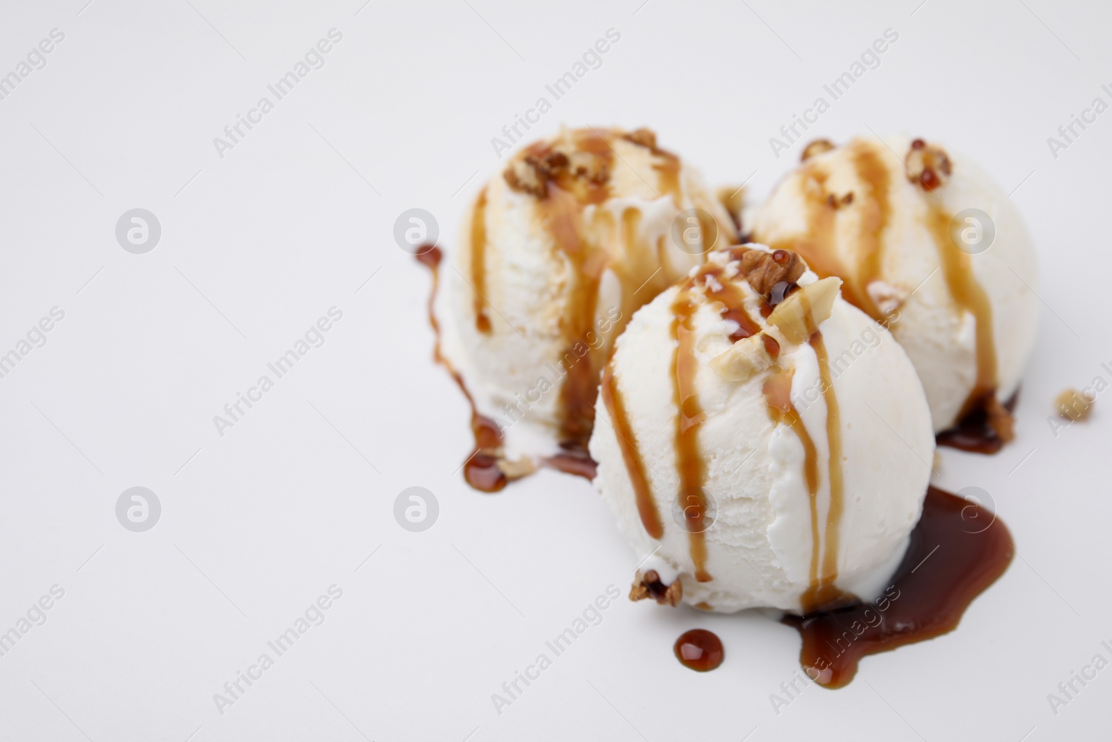 Photo of Scoops of ice cream with caramel sauce and nuts on white background, closeup. Space for text