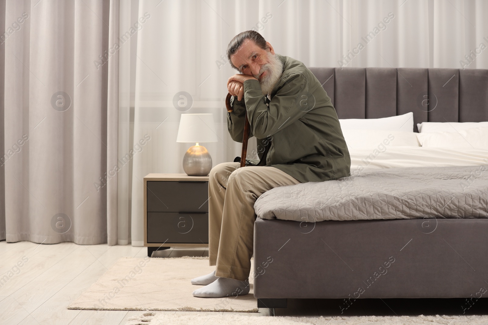 Photo of Senior man with walking cane on bed at home