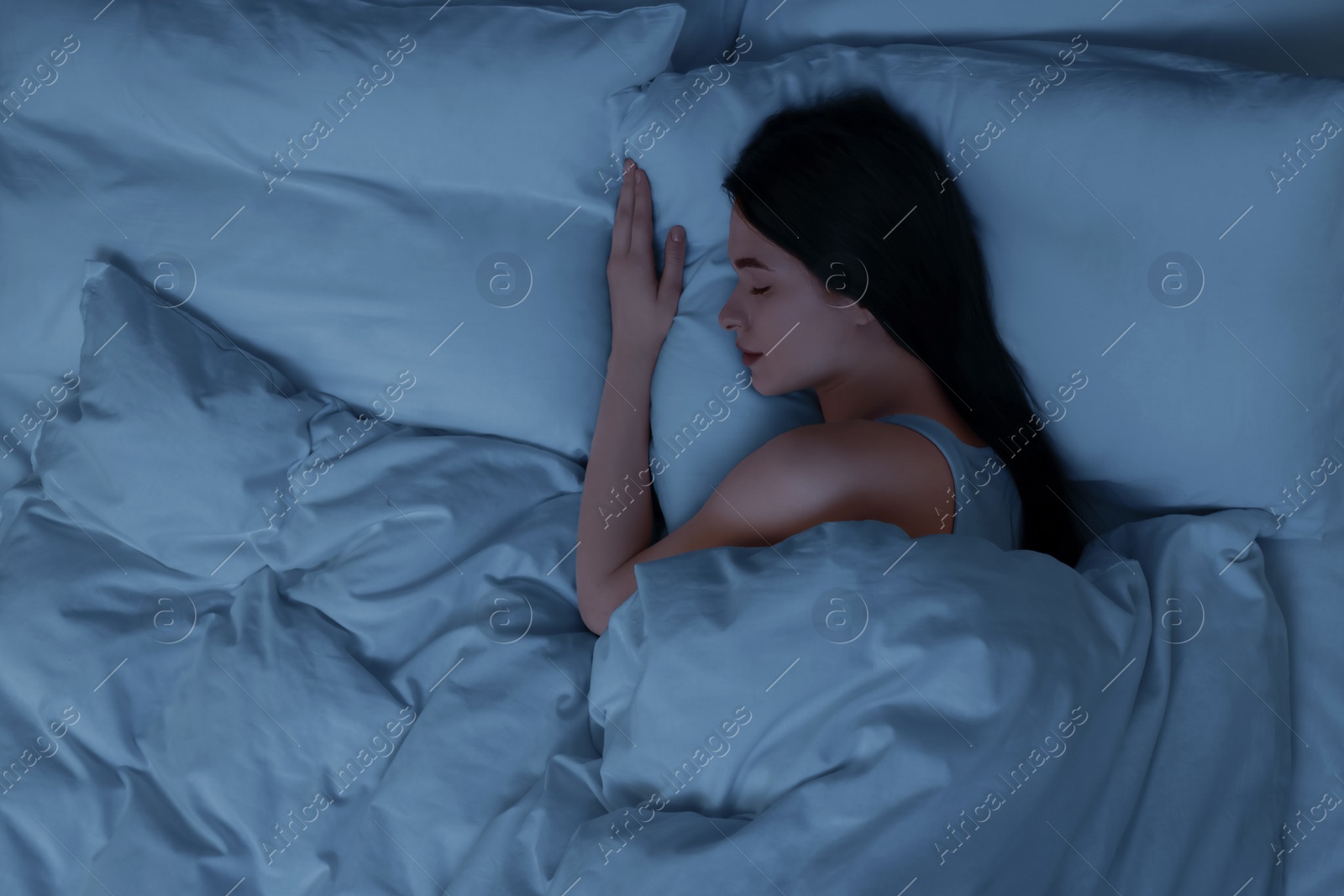 Photo of Beautiful young woman sleeping in bed at night, top view