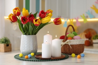 Easter decorations. Bouquet of tulips, painted eggs and burning candles on table indoors, closeup