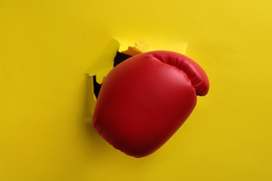 Photo of Man breaking through yellow paper with boxing glove, closeup