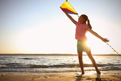 Cute little child playing with kite on beach near sea at sunset. Spending time in nature