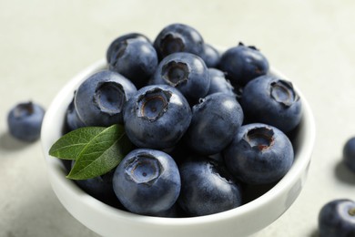 Photo of Bowl of fresh tasty blueberries on light grey table, closeup