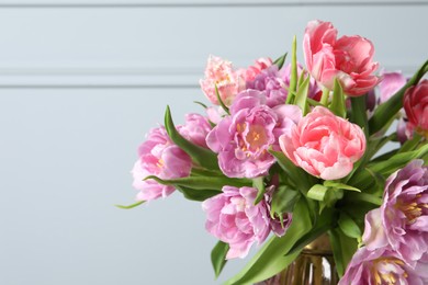 Photo of Beautiful bouquet of colorful tulip flowers against light grey wall, closeup. Space for text