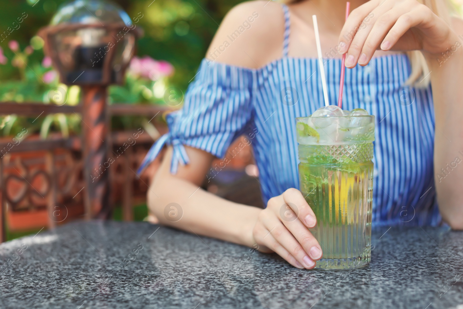 Photo of Young woman with glass of tasty lemonade at table in cafe, outdoors. Natural detox drink