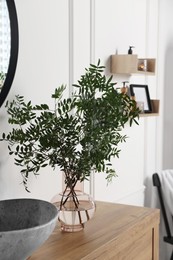 Photo of Eucalyptus branches near vessel sink on bathroom vanity. Interior design