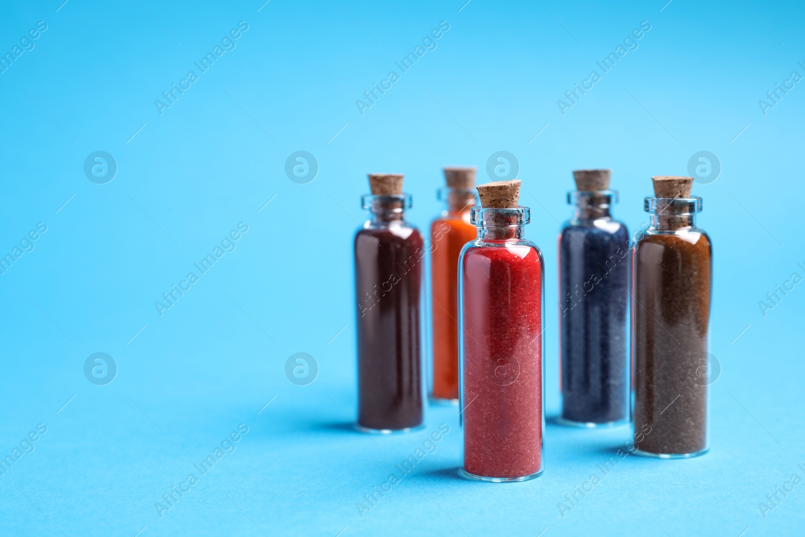 Photo of Glass bottles with different food coloring on light blue background. Space for text