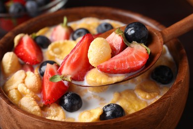 Photo of Spoon of crispy corn flakes with milk and berries above bowl, closeup