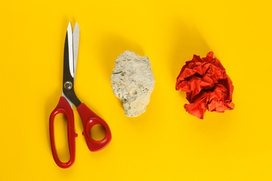 Flat lay composition with rock, paper and scissors on yellow background