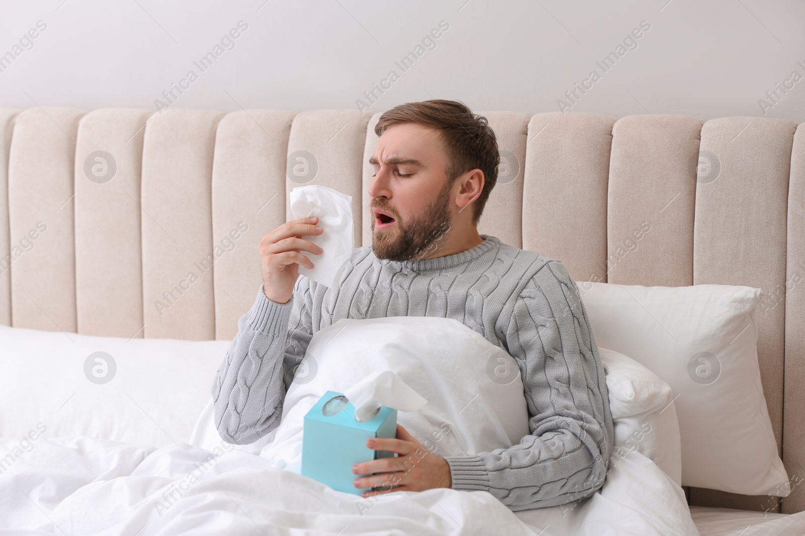 Photo of Young man suffering from runny nose in bed indoors