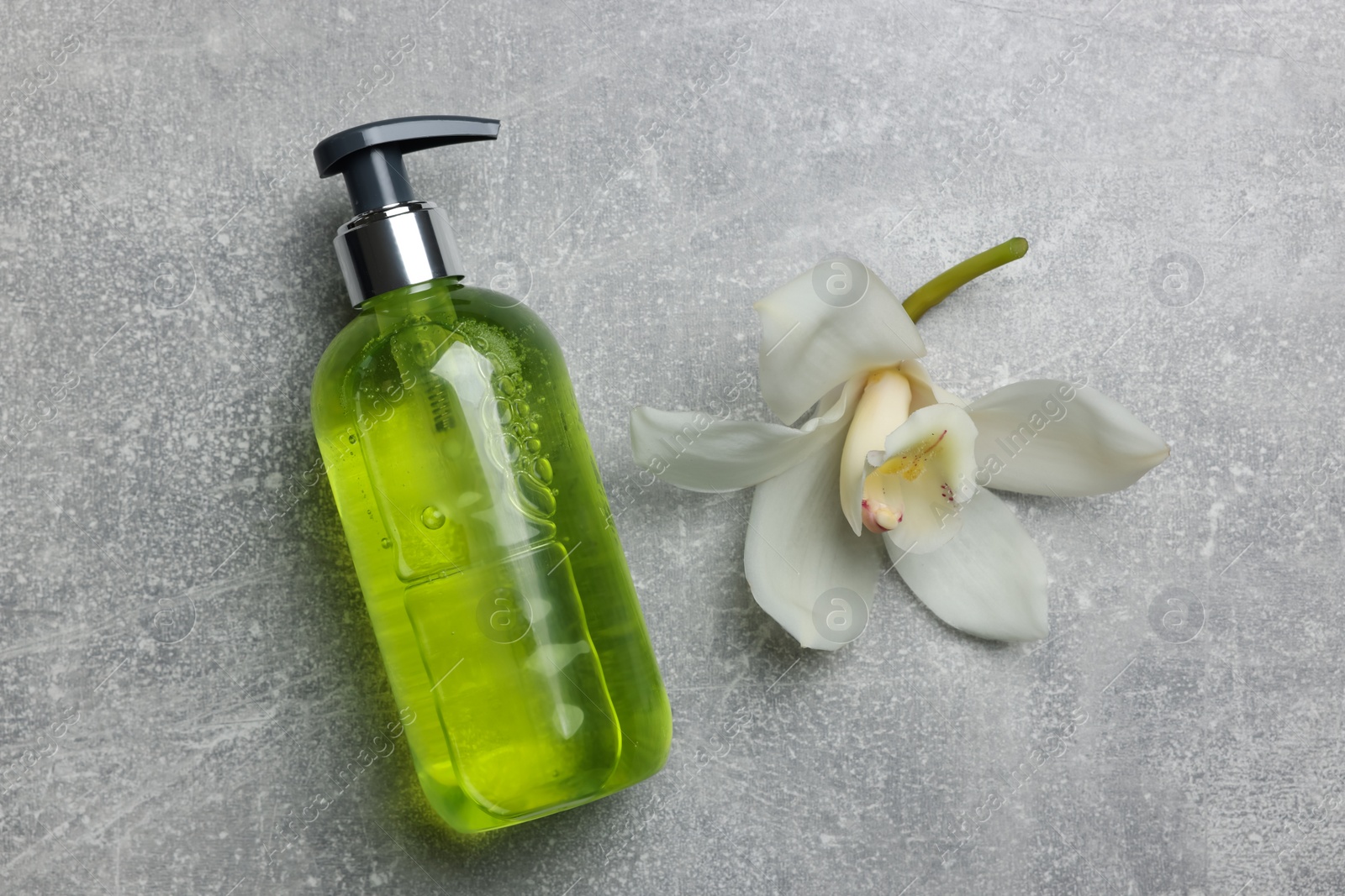 Photo of Dispenser of liquid soap and orchid flower on grey table, flat lay