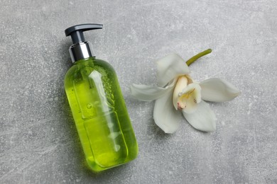 Dispenser of liquid soap and orchid flower on grey table, flat lay