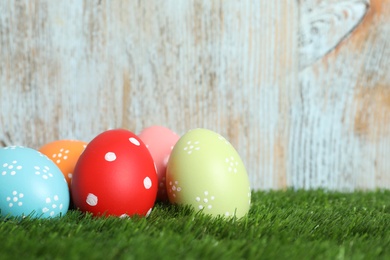 Photo of Colorful painted Easter eggs on green grass against wooden background, space for text