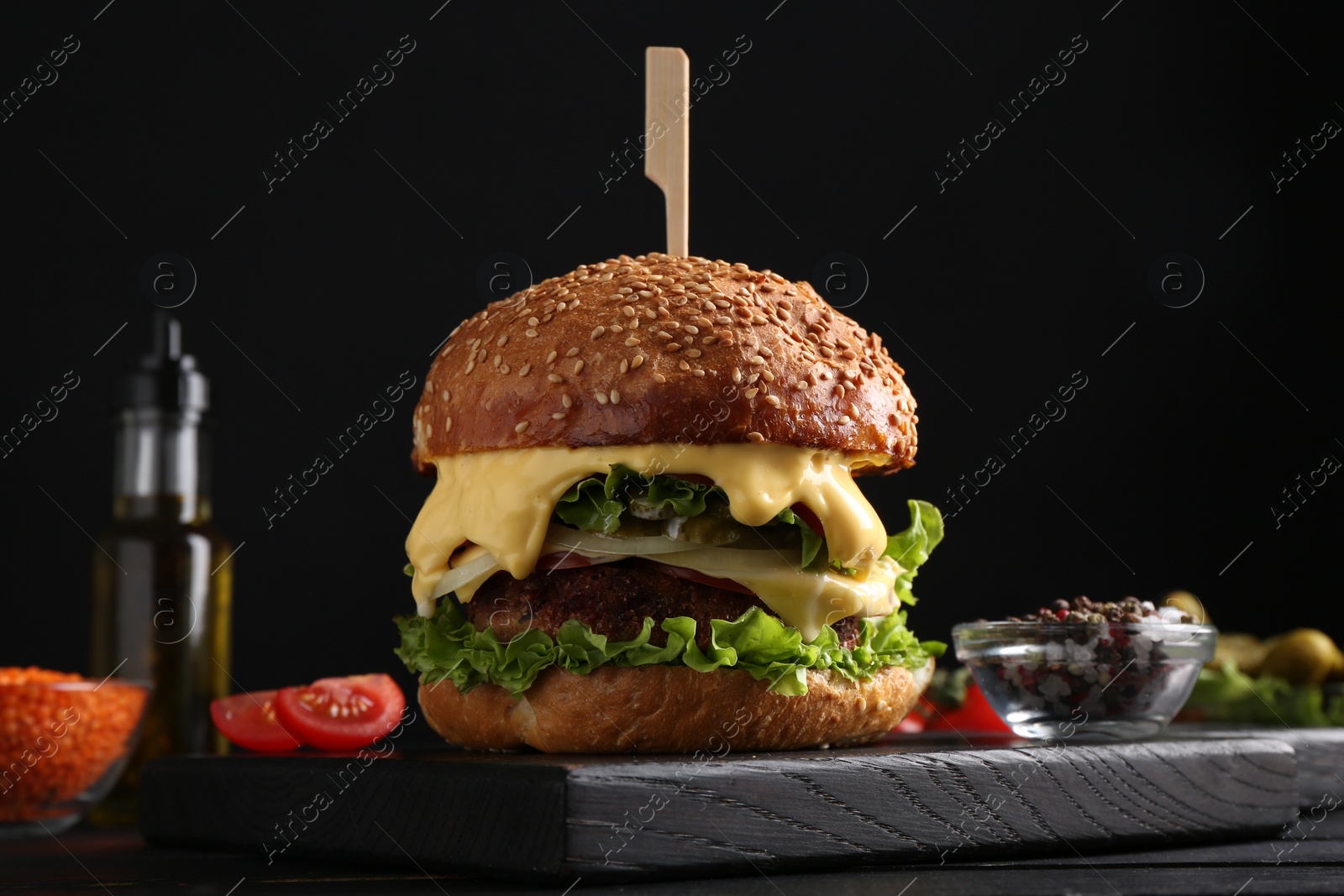 Photo of Vegetarian burger with delicious patty and cheese on black wooden table