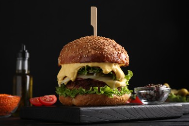 Photo of Vegetarian burger with delicious patty and cheese on black wooden table