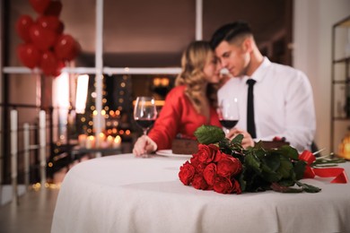 Lovely couple celebrating Valentine's day in restaurant, focus on table with red roses