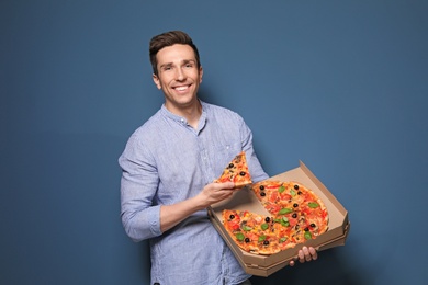 Attractive young man with delicious pizza on color background