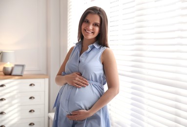 Young pregnant woman near window at home