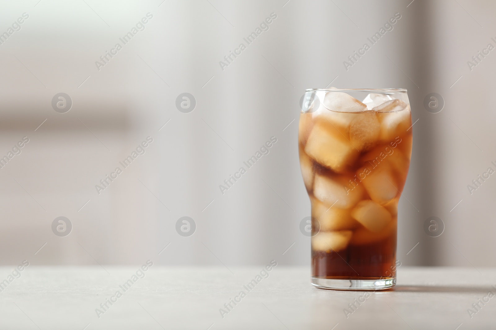 Photo of Glass of cola with ice on table against blurred background, space for text