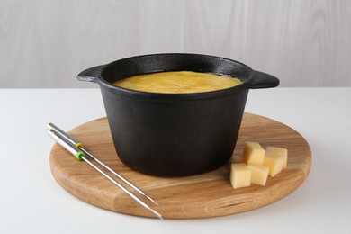 Fondue with tasty melted cheese and forks on white table