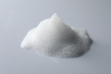Photo of Drop of fluffy soap foam on light grey background