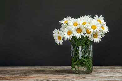 Vase with beautiful chamomile flowers on table against dark background