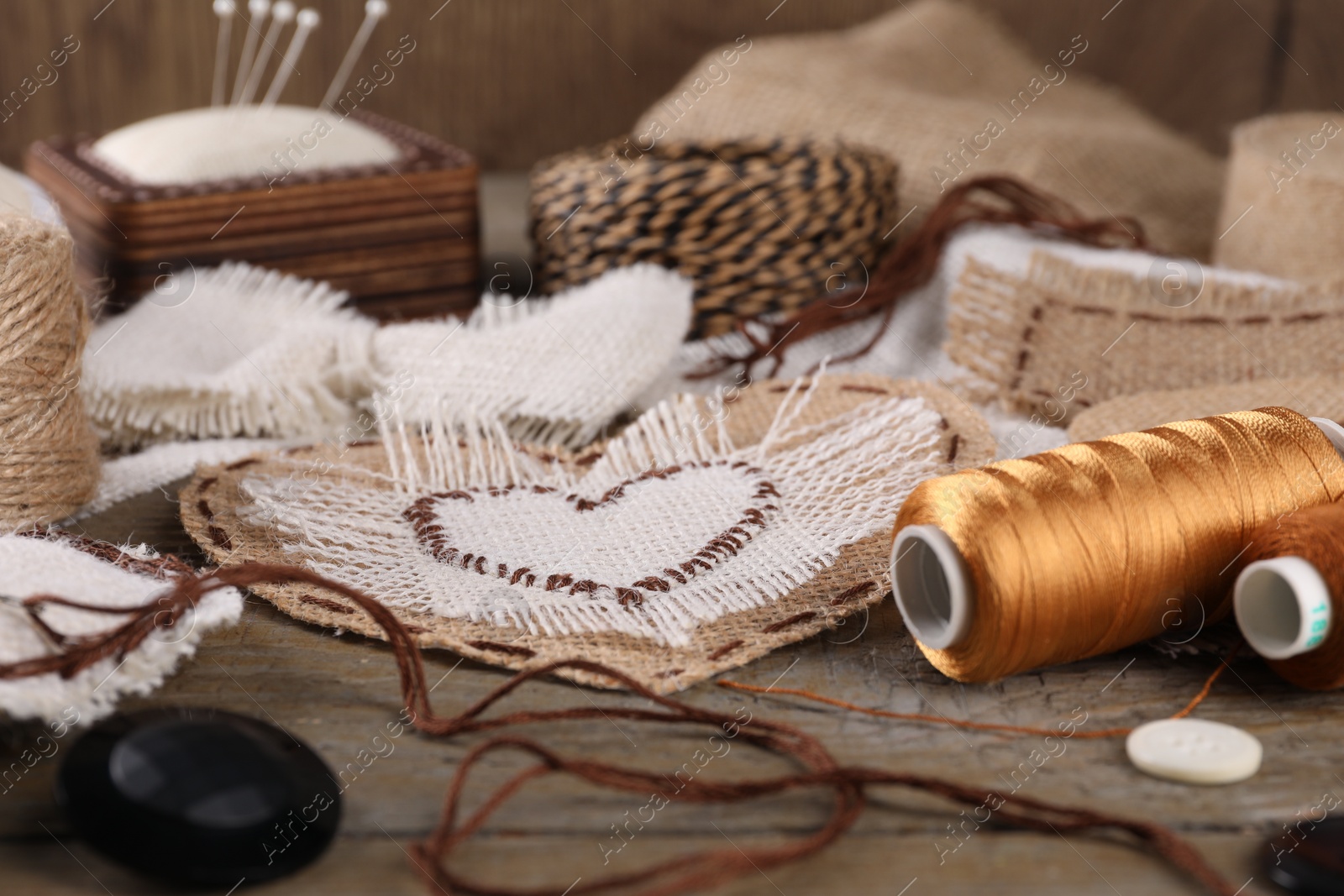 Photo of Pieces of burlap fabric with different stitches and sewing tools on wooden table