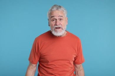 Portrait of surprised senior man on light blue background