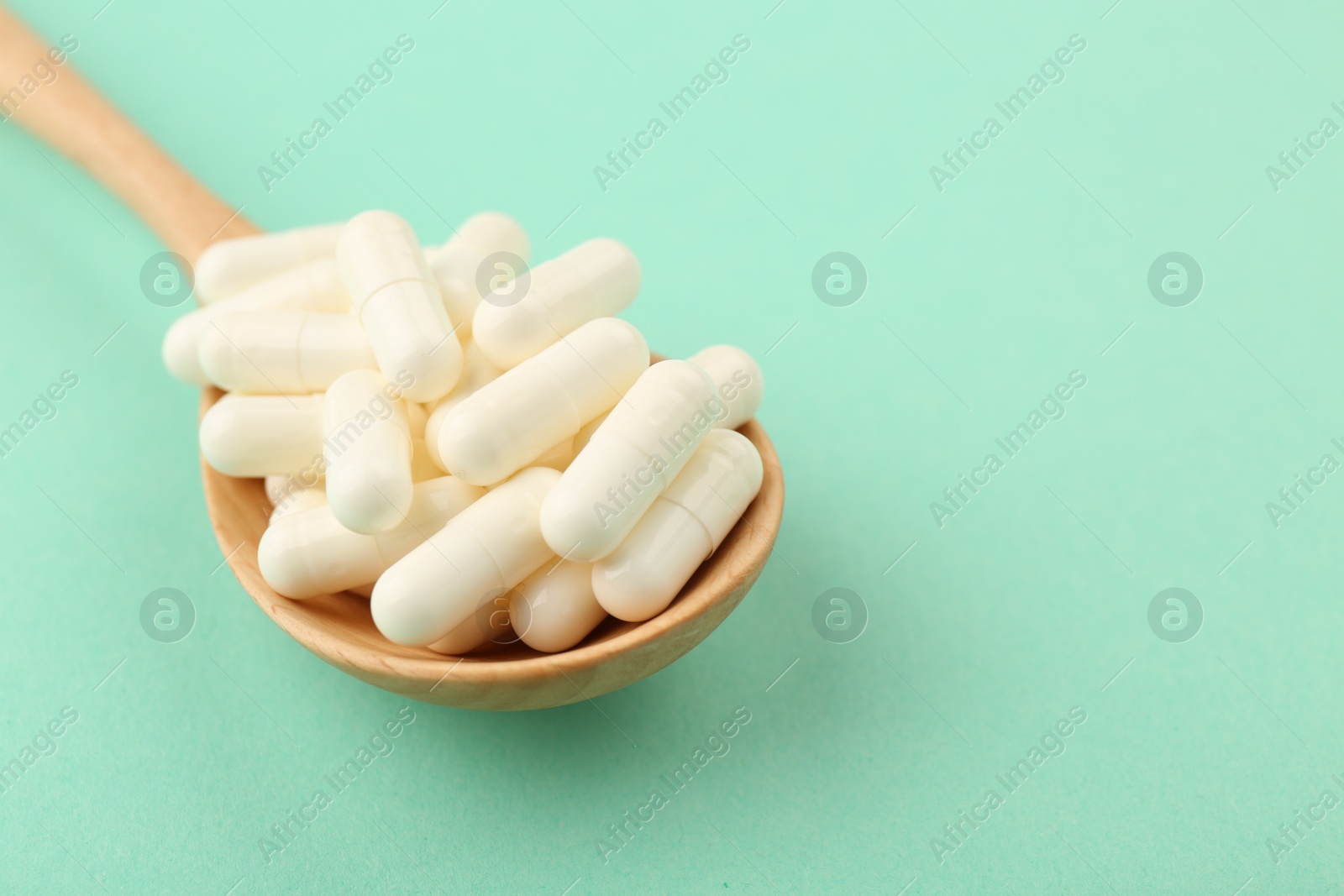 Photo of Wooden spoon with vitamin capsules on turquoise background, closeup. Space for text