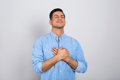 Handsome grateful man with hands on chest against light grey background