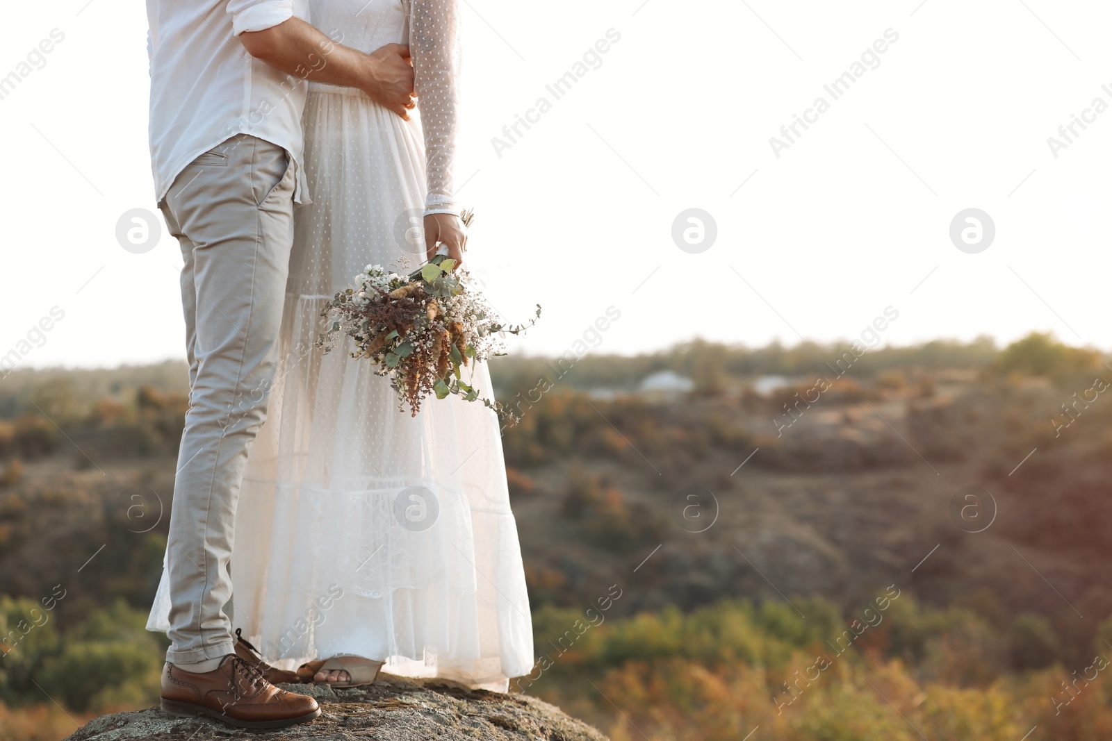 Photo of Happy newlyweds with beautiful field bouquet outdoors, closeup