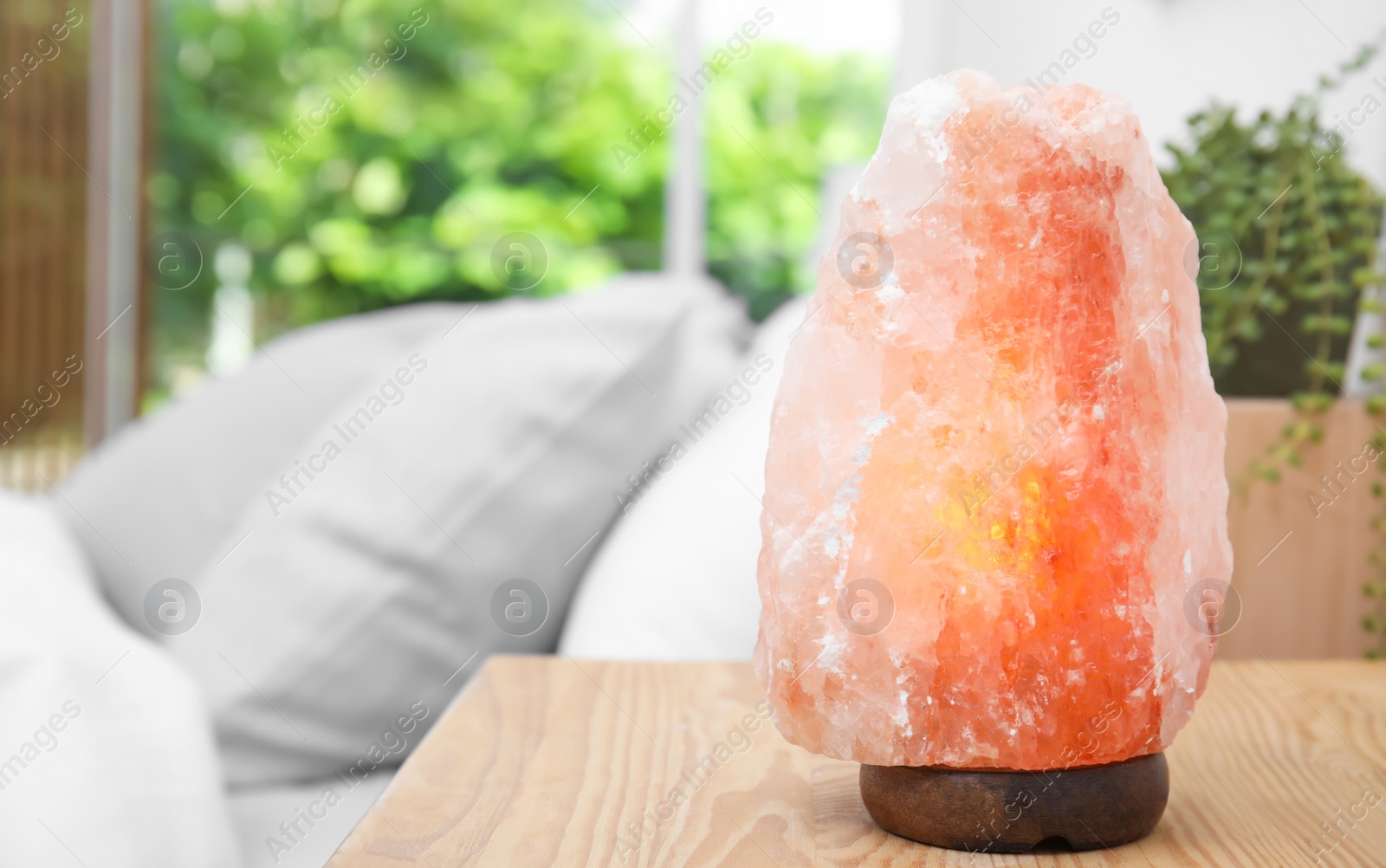 Photo of Himalayan salt lamp on wooden table in bedroom. Space for text