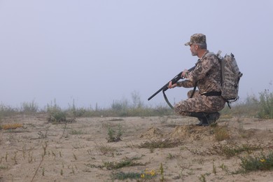 Man wearing camouflage with hunting rifle outdoors. Space for text