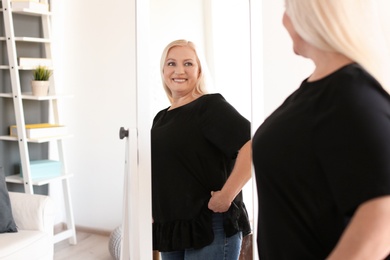 Photo of Mature woman looking in mirror at home
