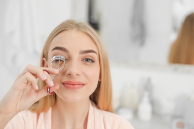 Attractive young woman curling her eyelashes indoors