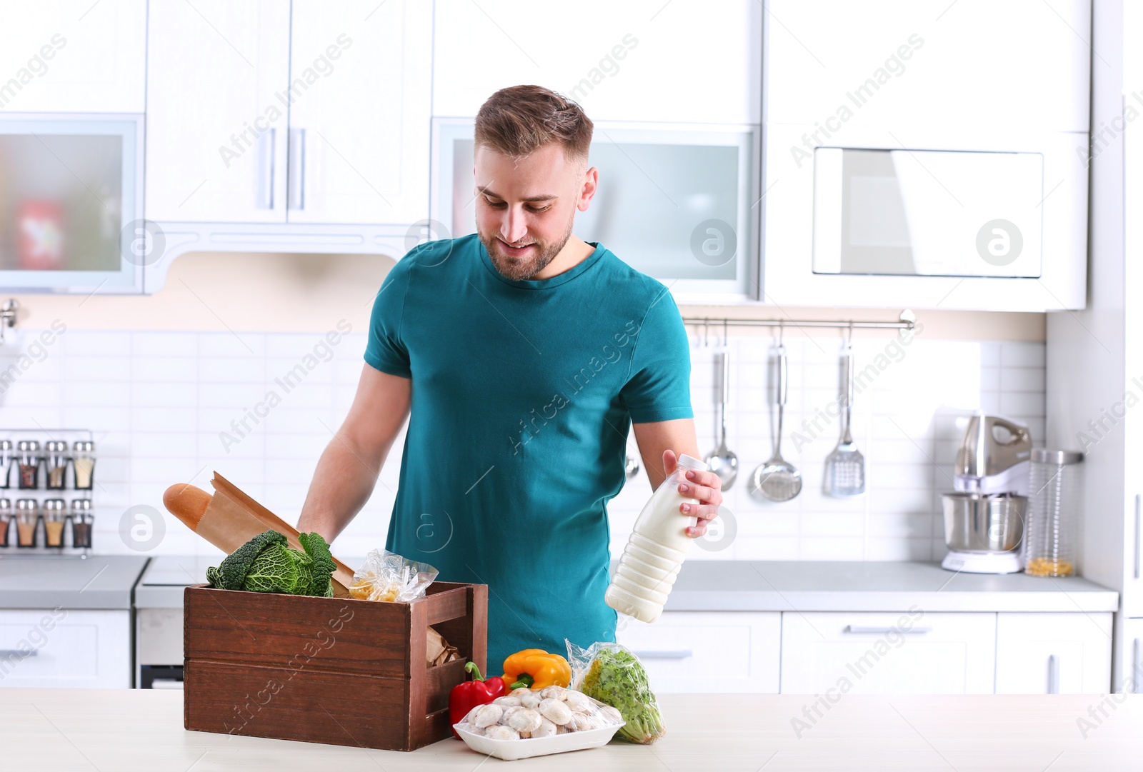 Photo of Young man with wooden crate full of products at table in kitchen. Food delivery service