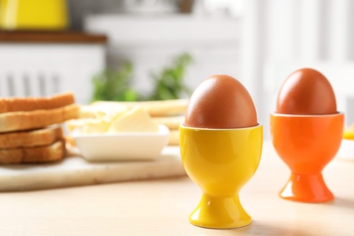 Cups with boiled eggs on wooden table, space for text. Healthy breakfast