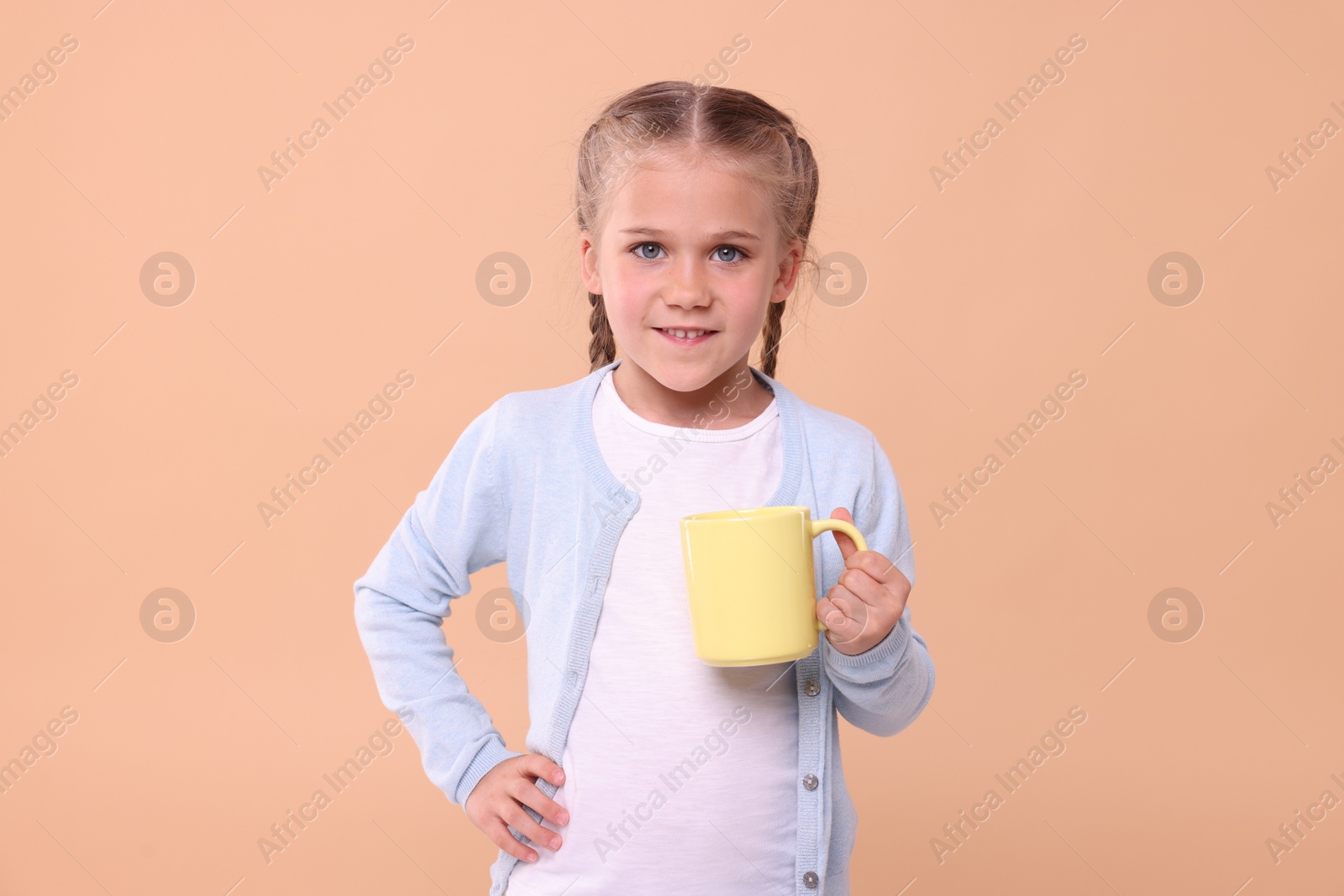 Photo of Happy girl with yellow ceramic mug on beige background