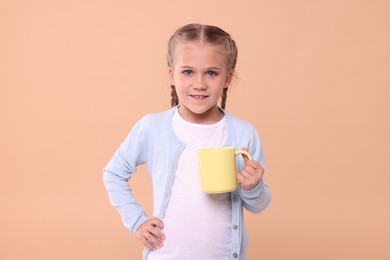 Happy girl with yellow ceramic mug on beige background