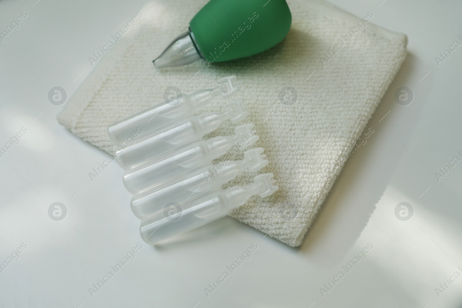 Photo of Single dose ampoules of sterile isotonic sea water solution, towel and nasal aspirator on white table