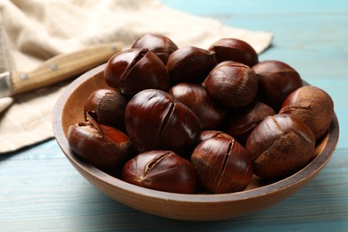 Photo of Fresh edible sweet chestnuts in bowl on light blue wooden table