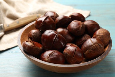 Fresh edible sweet chestnuts in bowl on light blue wooden table