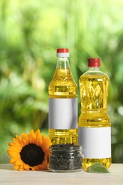 Photo of Bottles of sunflower cooking oil, seeds and yellow flower on white wooden table outdoors