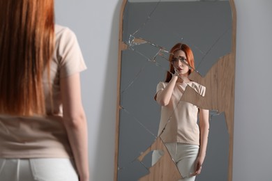 Mental problems. Depressed woman reflecting in broken mirror indoors
