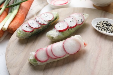 Photo of Delicious spring rolls, sesame seeds, green onion and carrots on table