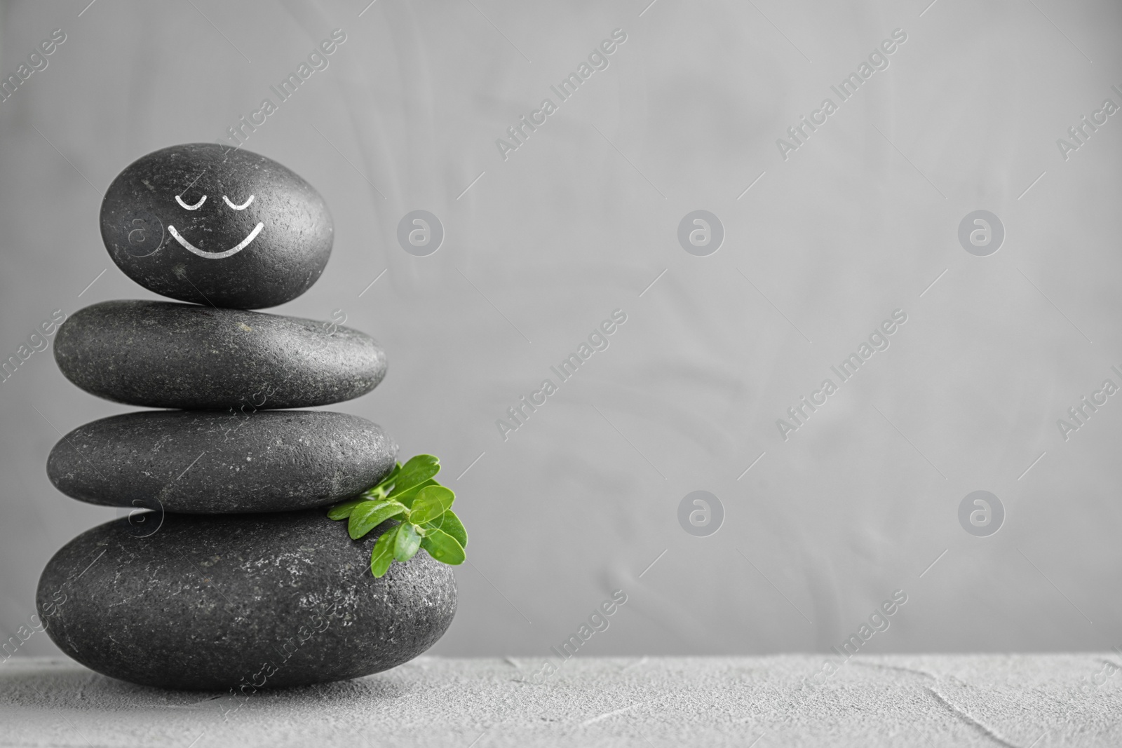 Image of Stack of stones with drawn happy face on light grey table, space for text. Be in harmony and enjoying your life