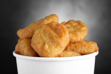 Photo of Bucket with delicious chicken nuggets on grey background, closeup