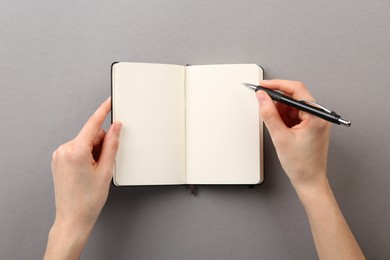 Photo of Woman writing in notebook on grey background, top view