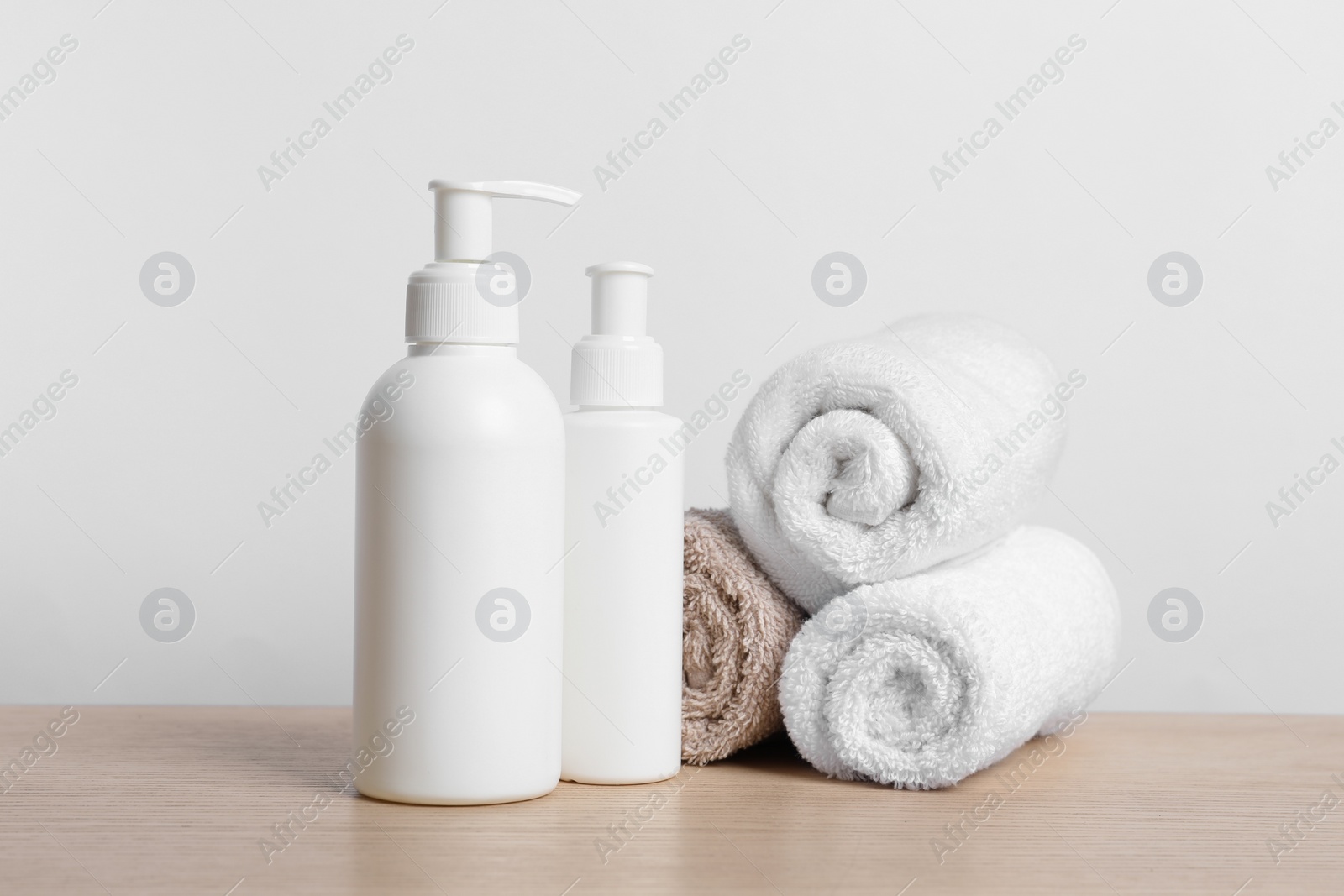 Photo of Bottles of cosmetic products and rolled towels on wooden table