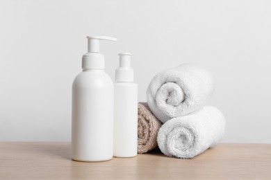 Bottles of cosmetic products and rolled towels on wooden table